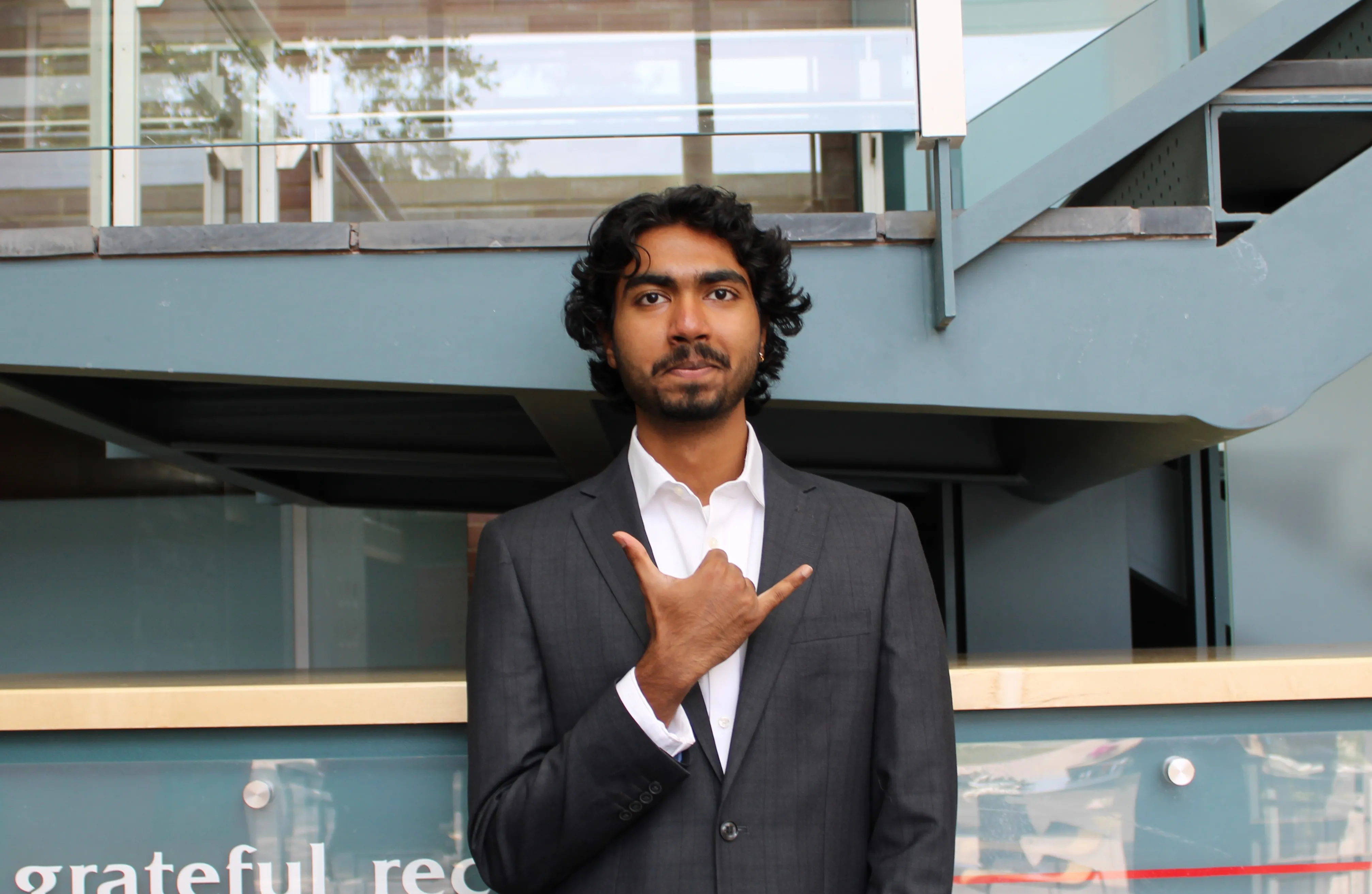 Sanjit in a suit, throwing a shaka
